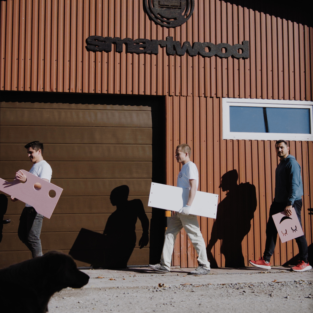 Pracownicy przechodzący przed halą produkcyjną Smartwood trzymający drewniane części łóżek i mebli dziecięcych